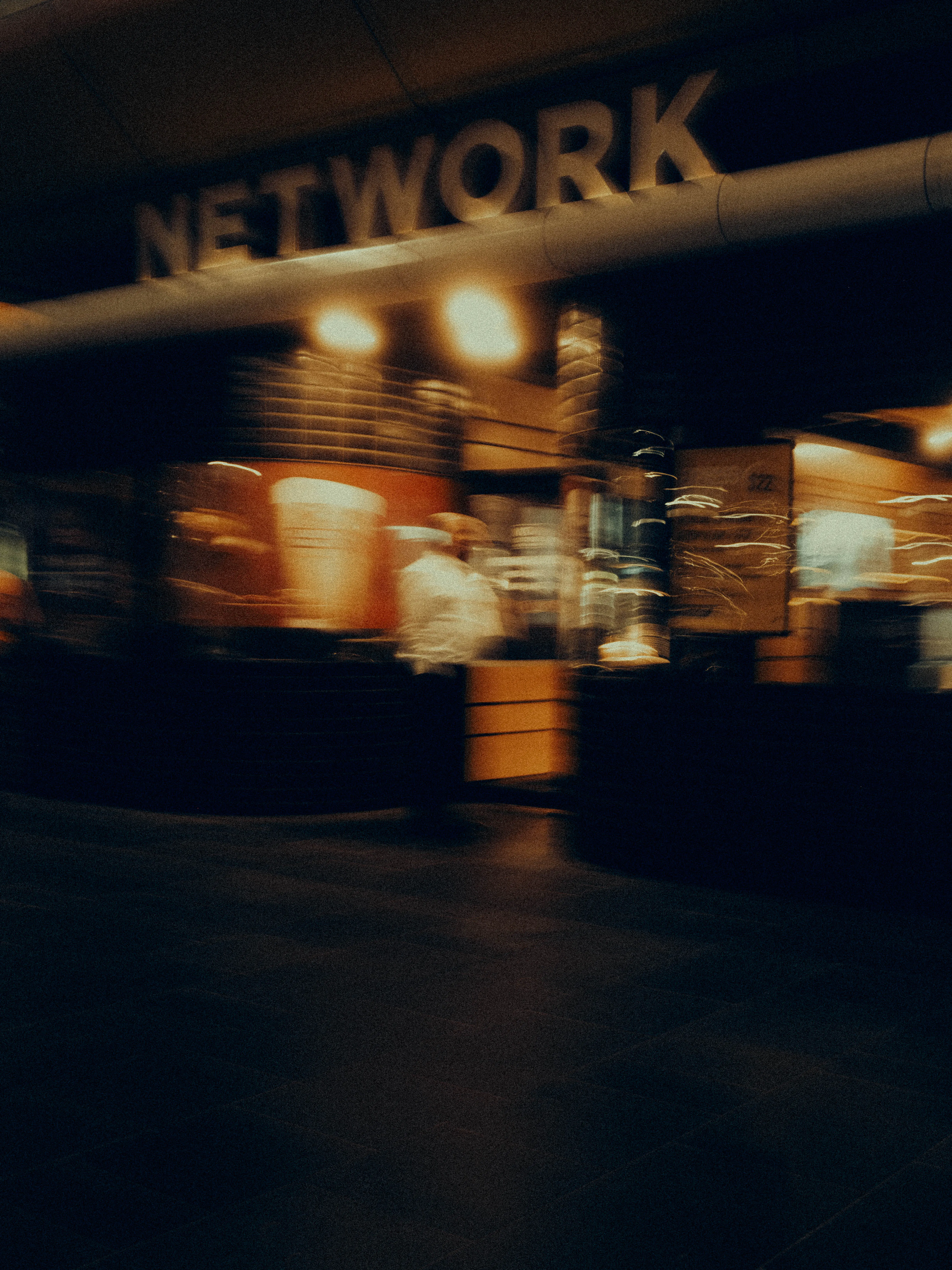 A venue glowing with the word "Network" in warm amber recedes into motion blur, patrons and pendant lights merging into an abstract cinematic impression of inner-city nightlife.