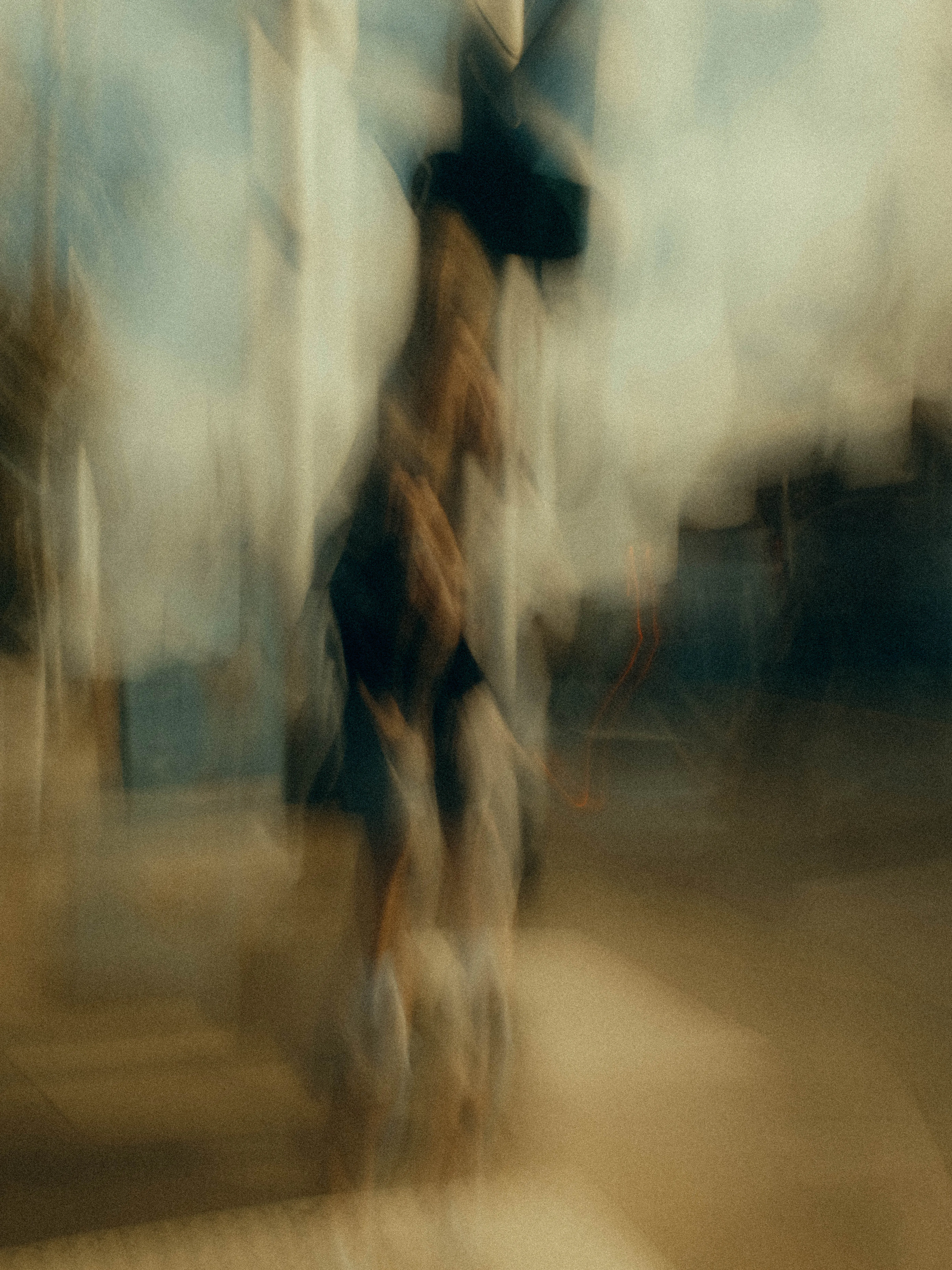 A figure in dark shorts navigates a bright hazy streetscape, dissolving into pale columns of diffused light and blurred shopfronts under a wide, bleached sky.